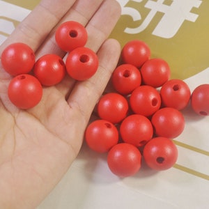 May include: A hand holding a pile of bright red wooden beads with a hole in the center of each bead.