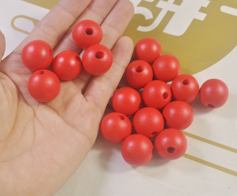 May include: A hand holding a pile of bright red wooden beads with a hole in the center of each bead.