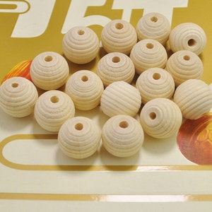 May include: A group of 17 natural wood beads with a grooved texture. The beads are arranged in a heart shape on a yellow and white background.