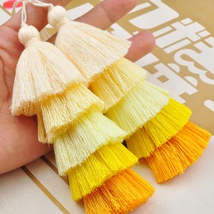 May include: Multi-layered tassel with a gradient of yellow, white and cream colours. The tassel is made of soft, fluffy fibres and has a delicate, layered design.