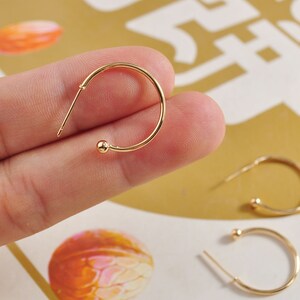 May include: Gold hoop earrings with a small ball at the end of each hoop.