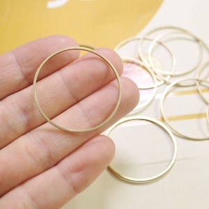 May include: A close-up of a gold-colored metal ring, with a smooth, polished finish. The ring is held in a hand, and there are several other similar rings in the background.