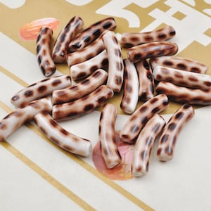 May include: A collection of brown and white patterned ceramic beads. The beads are shaped like curved cylinders and have a mottled brown and white pattern.