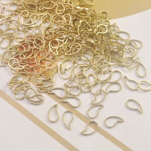 May include: A large pile of gold-colored metal teardrop shapes. The teardrops are scattered on a white and brown striped surface.