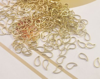 May include: A large pile of gold-colored metal teardrop shapes. The teardrops are scattered on a white and brown striped surface.
