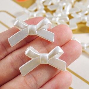 Può includere: Primo piano di una mano che tiene due fiocchi di plastica bianca. I fiocchi sono larghi circa 2,5 cm e hanno una finitura perlata.