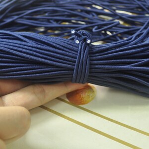 May include: A close-up of a large spool of navy blue elastic cord. The cord is tightly wound and has a white knot at the end.
