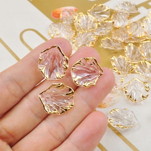 May include: A set of clear glass rose petals with gold trim. The petals are arranged on a hand and a table.