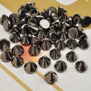 May include: A large group of black metal pyramid studs. The studs have a shiny finish and are scattered on a white and gold surface.