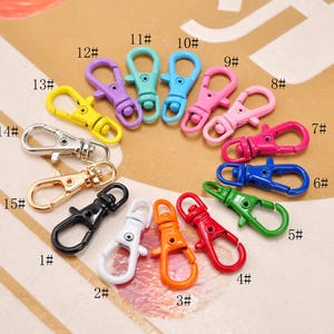May include: A collection of colorful metal lobster clasp keychains in various colors, including yellow, purple, teal, blue, pink, red, green, orange, silver, gold, black, and white. Each clasp is numbered.