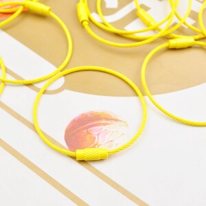 May include: A close-up of a yellow cable tie with a metal clasp. The cable tie is lying on a white and brown surface.