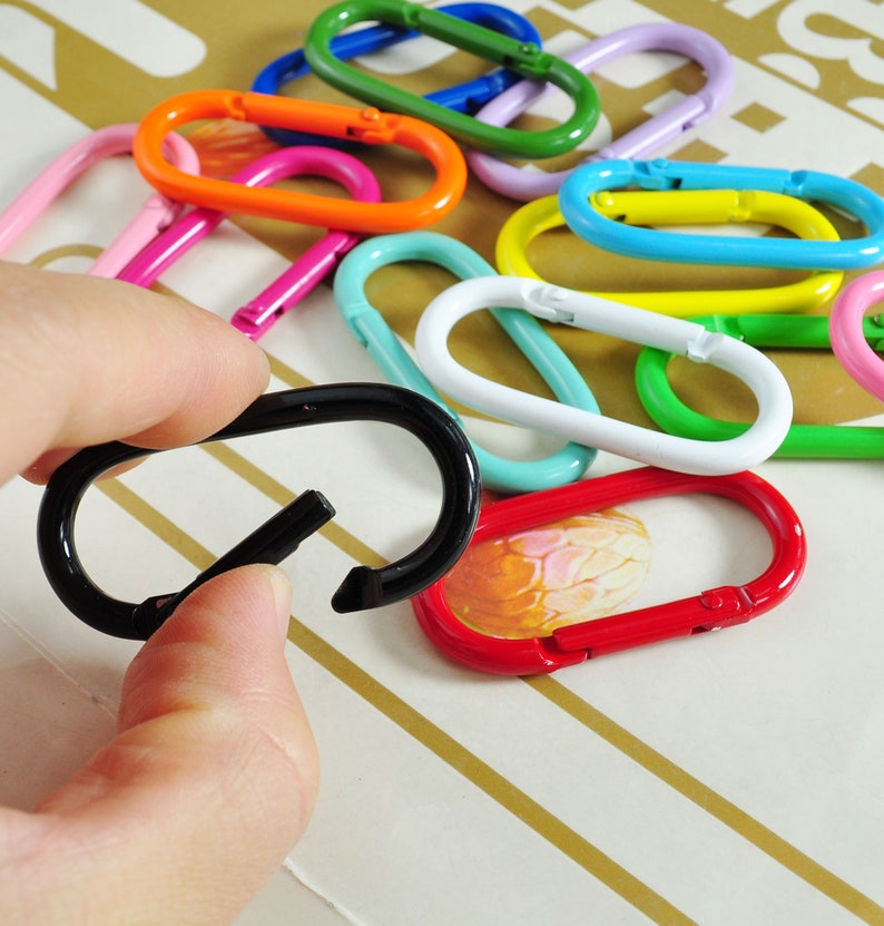 May include: A collection of colorful metal key rings in various shapes and sizes, including a black key ring held in a hand.