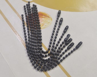 Puede incluir: Un conjunto de diez cadenas de metal negro con un bucle en un extremo. Las cadenas están hechas de pequeñas cuentas redondas.