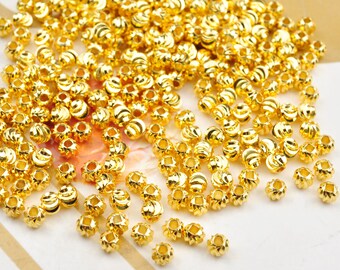 May include: A large pile of gold-colored metal beads with a ridged design. The beads are scattered on a white surface.