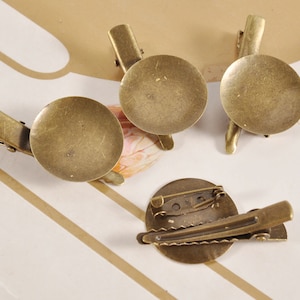 May include: Four antique gold-toned metal blank round cameo brooch clips. Each clip has a round metal base with a smooth, slightly textured surface. The clips are designed to hold a cameo or other decorative element.