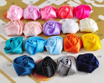 May include: Assortment of 19 small satin fabric rose flower embellishments in various colors, including pink, blue, purple, white, yellow, orange, and black.