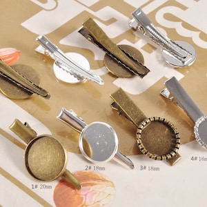 May include: A collection of metal hair clips with round, flat bases in various sizes. The clips are in silver and bronze tones, with some featuring decorative edges. Sizes are labeled as 16mm, 18mm, and 20mm.