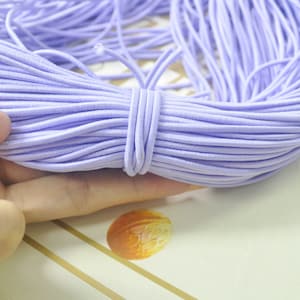 May include: A large spool of lavender elastic string. The string is wound tightly and is ready to be used for crafts or sewing projects.