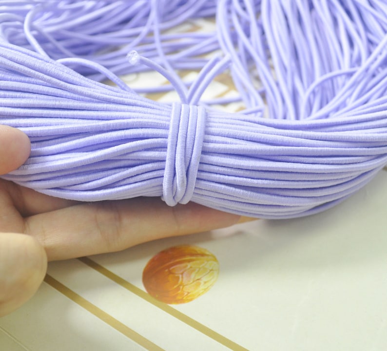 May include: A large spool of lavender elastic string. The string is wound tightly and is ready to be used for crafts or sewing projects.