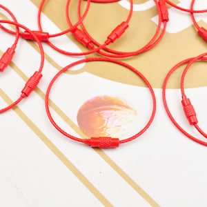 May include: A close-up of a group of red cable keyrings with red plastic end caps. The keyrings are arranged on a light brown surface.