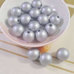 May include: A bowl filled with silver wooden beads. The beads are round and smooth, and they have a shiny finish.