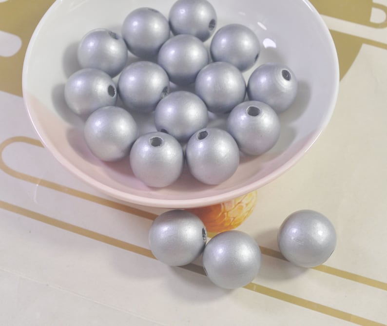 May include: A bowl filled with silver wooden beads. The beads are round and smooth, and they have a shiny finish.