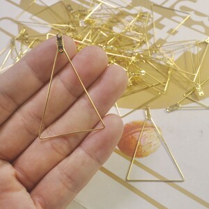 May include: A close-up of a gold triangle-shaped wire frame. The frame is held in a hand, and there are many other similar frames in the background.