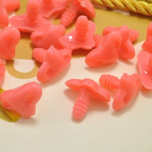 May include: A collection of pink plastic safety eyes with screw backs. The eyes are in various shapes and sizes, and some have a heart shape.