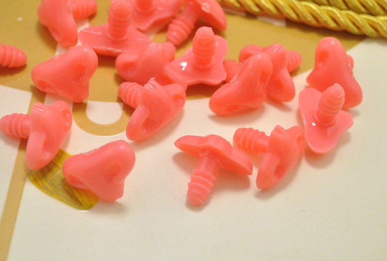 May include: A collection of pink plastic safety eyes with screw backs. The eyes are in various shapes and sizes, and some have a heart shape.