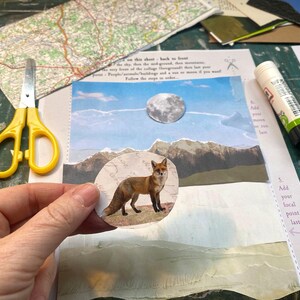 May include: A collage project featuring a circular cutout of a red fox held in the foreground. The background includes a mountain landscape, a moon, yellow scissors, and a glue stick on a printed instruction sheet with text.