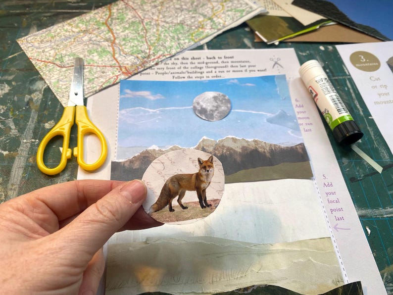 May include: A collage project featuring a circular cutout of a red fox held in the foreground. The background includes a mountain landscape, a moon, yellow scissors, and a glue stick on a printed instruction sheet with text.