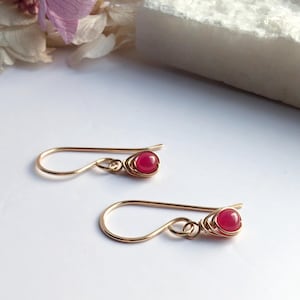 May include: A pair of gold earrings with small, round, pink gemstones. The earrings are made with wire wrapped around the gemstones.