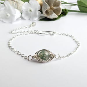 May include: A silver chain bracelet featuring a green moss agate stone wrapped in silver wire.