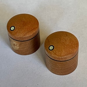 Puede incluir: Dos pequeñas cajas de madera con un acabado marrón claro. Cada caja tiene un borde negro alrededor de la parte superior y un círculo blanco con un contorno negro en la tapa.