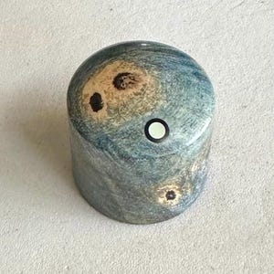 Puede incluir: Un pomo de madera azul, marrón y blanco con una incrustación negra y blanca. El pomo tiene un patrón de espiral.