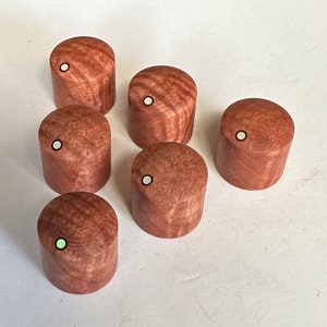 Peut inclure: Six boutons en bois avec un point blanc au centre. Les boutons sont de couleur brun rougeâtre avec un motif de grain de bois.