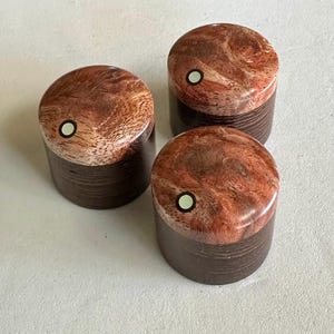 以下が含まれることがあります： 赤と茶色のマーブル模様と中央に白い点がついた木製ノブが3つ。ノブは丸型で、濃い茶色のベースがあります。