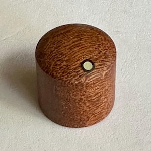 Könnte beinhalten: Ein Holzgriff mit einer weißen Einlage in der Mitte. Der Griff hat eine rotbraune Farbe und ein Holzmaserungsmuster.