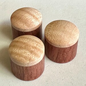 Puede incluir: Tres pomos de madera con la parte superior de color marrón claro y la parte inferior de color marrón rojizo oscuro.