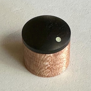 May include: A wooden knob with a black top and a white dot in the center. The bottom of the knob is a light brown wood with a wood grain pattern.