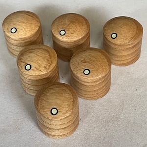 May include: Six wooden knobs with a light brown finish and a white dot in the center. The knobs are arranged in a circle on a white surface.