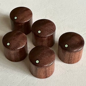 Könnte beinhalten: Fünf braune Holzknöpfe mit einem weißen Punkt in der Mitte. Die Knöpfe sind rund und haben eine glatte Oberfläche.
