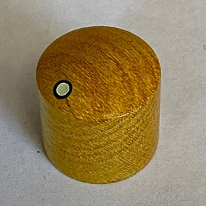 Könnte beinhalten: Ein Holzgriff mit einem weißen und schwarzen Kreis auf der Oberseite. Der Griff ist hellbraun und hat eine Holzmaserung.