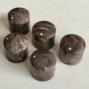 Puede incluir: Cinco pomos de guitarra de madera con un patrón de veta de madera marrón oscuro y morado y un punto blanco en el centro de cada pomo.