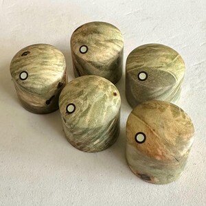 Puede incluir: Cinco pomos de madera con un patrón de mármol verde y marrón y un círculo blanco en el centro de cada pomo.