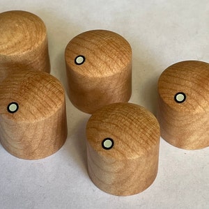 May include: Five wooden knobs with a white dot in the center. The knobs are a light brown color and have a wood grain pattern.
