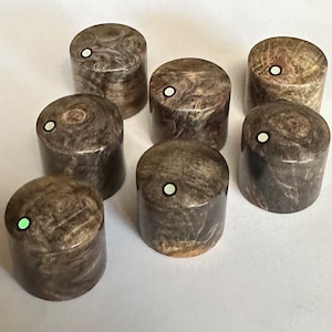 Puede incluir: Ocho pomos de madera con un patrón de mármol marrón oscuro y gris y un punto blanco en el centro.