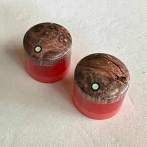 May include: Two small red resin containers with wooden lids. The lids have a brown and black marbled pattern with a white dot in the center.