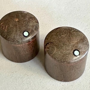 May include: Two brown cylindrical knobs with a light green dot on top. The knobs have a textured surface and a slightly angled top. The knobs are likely for a piece of audio equipment or a similar device.