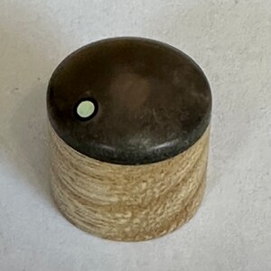 May include: A small wooden box with a dark brown lid and a light brown base. The lid has a small white circle in the center.